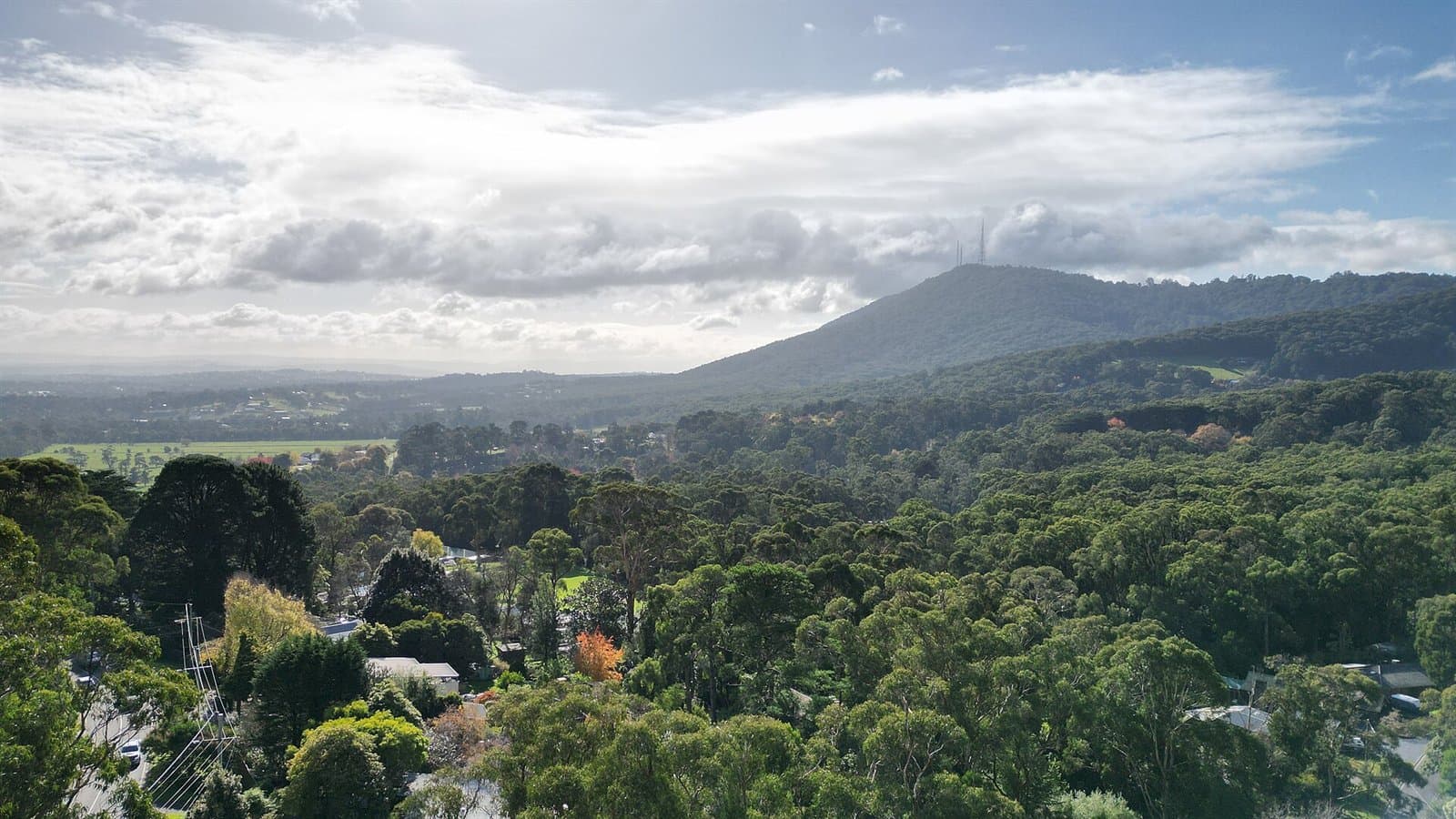 Forested foothills below a mountain with radio towers on its summit